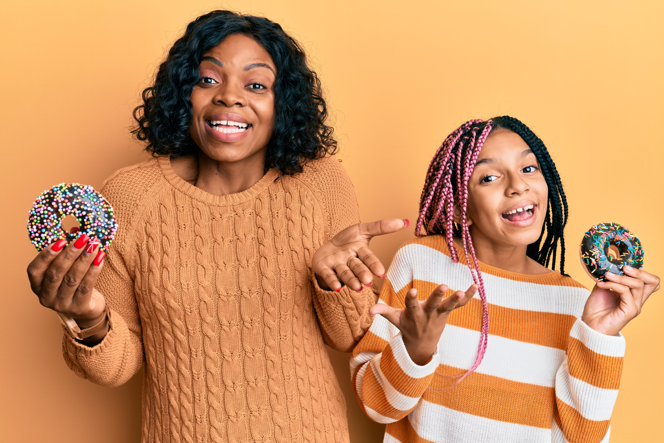 Beautiful african american mother and daughter holding donuts celebrating achievement with happy smile and winner expression with raised hand