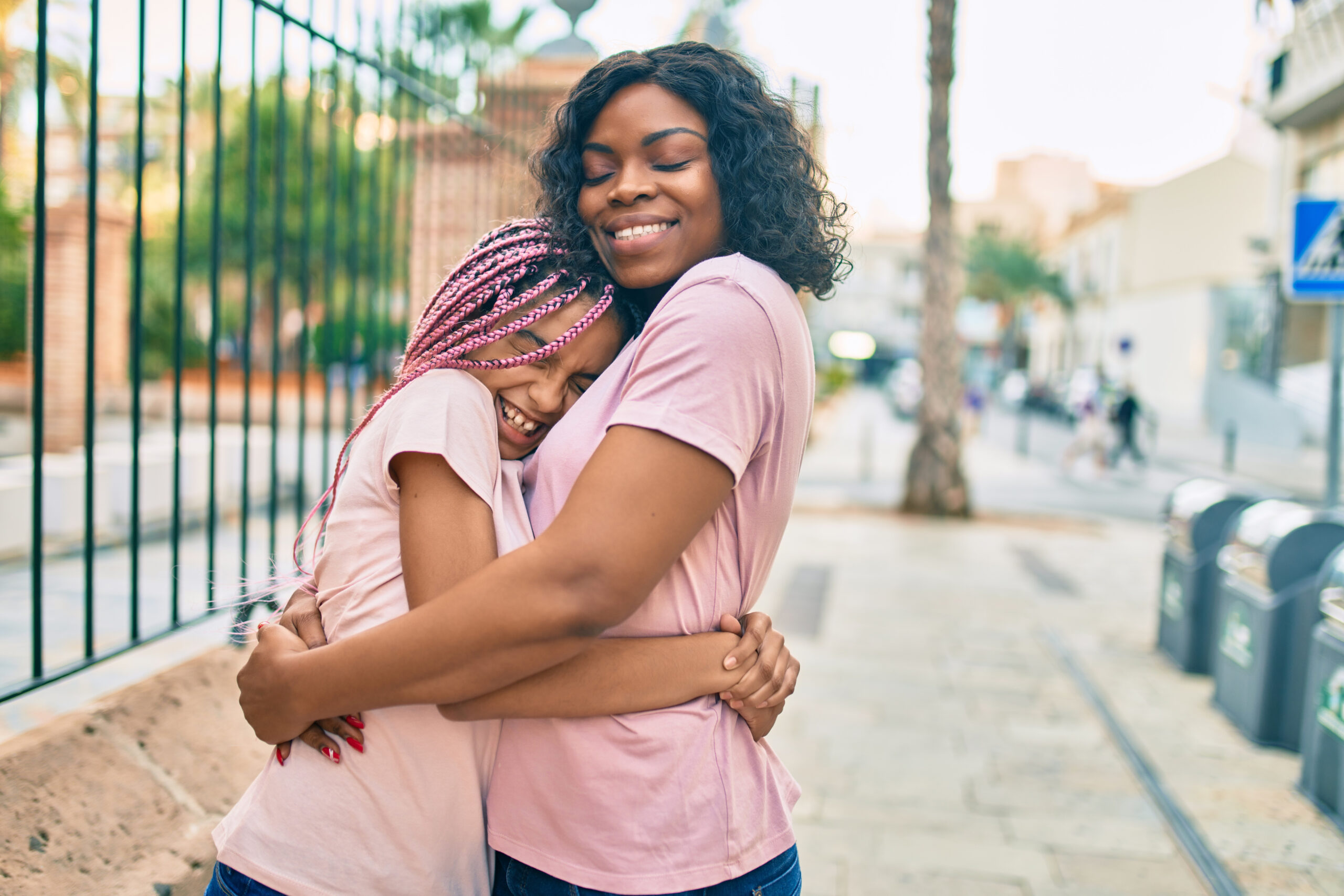 Beautiful african american mother and daughter smiling happy and hugging. Standing with smile on face standing at the city.