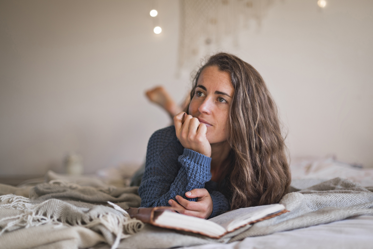 Woman lying on her bed thinking about what to write in her journal