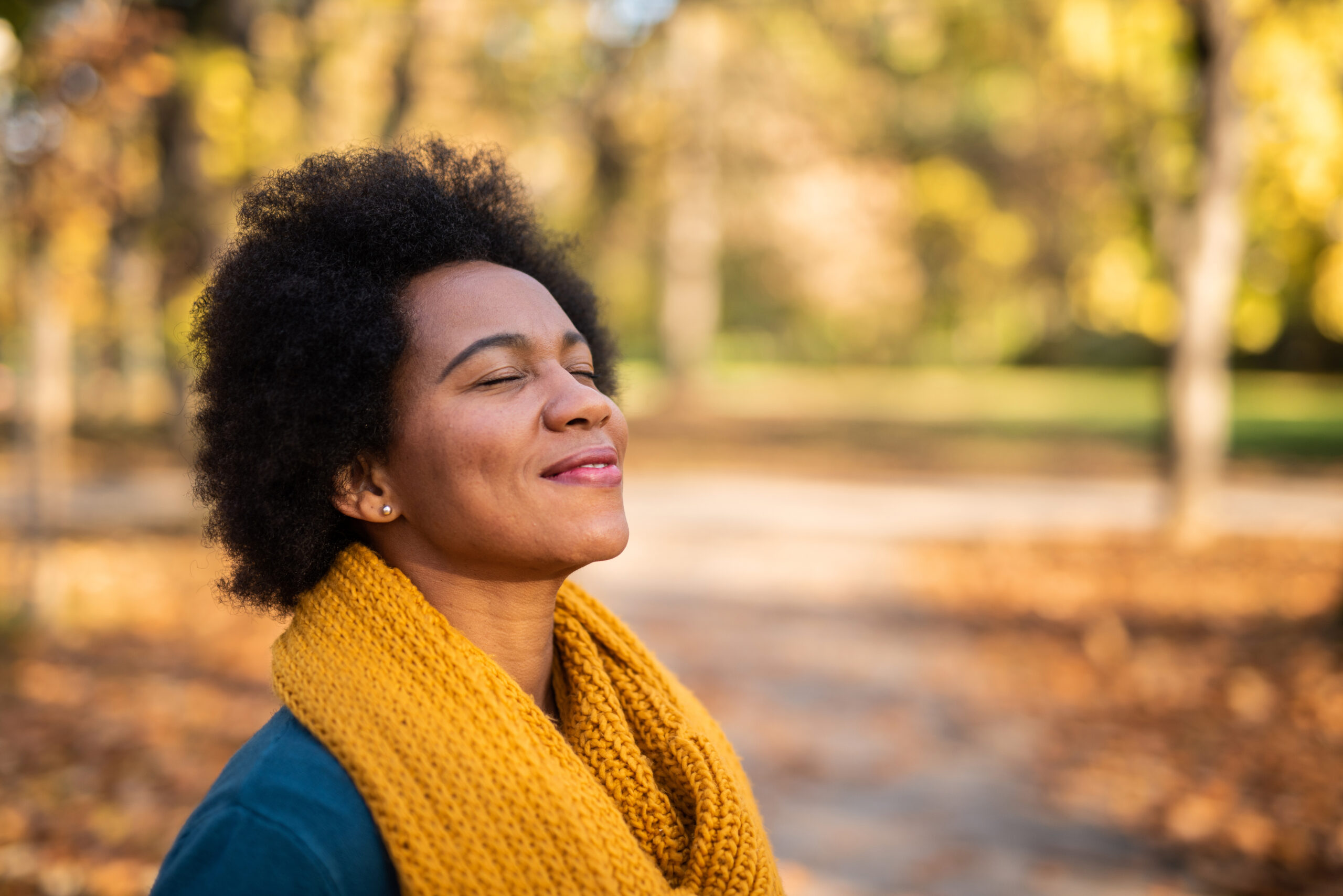 African American woman day dreaming in public park on beautiful autumn day.