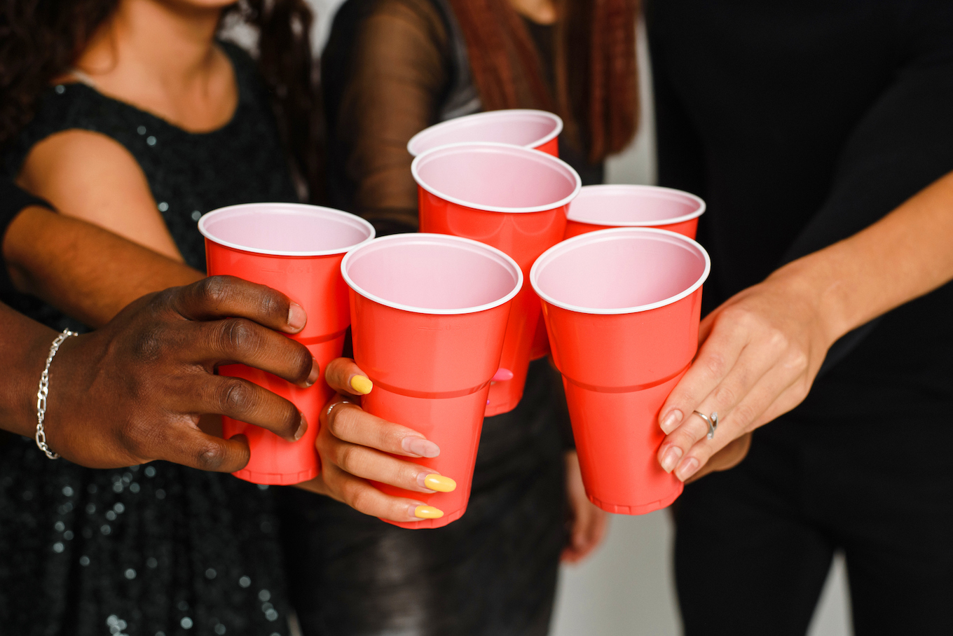 Waist up of six friends having fun and drinking alcohol during New Year party, isolated on white background. A group of cheerful friends of different nationalities clink glasses with red glasses at a party in the studio