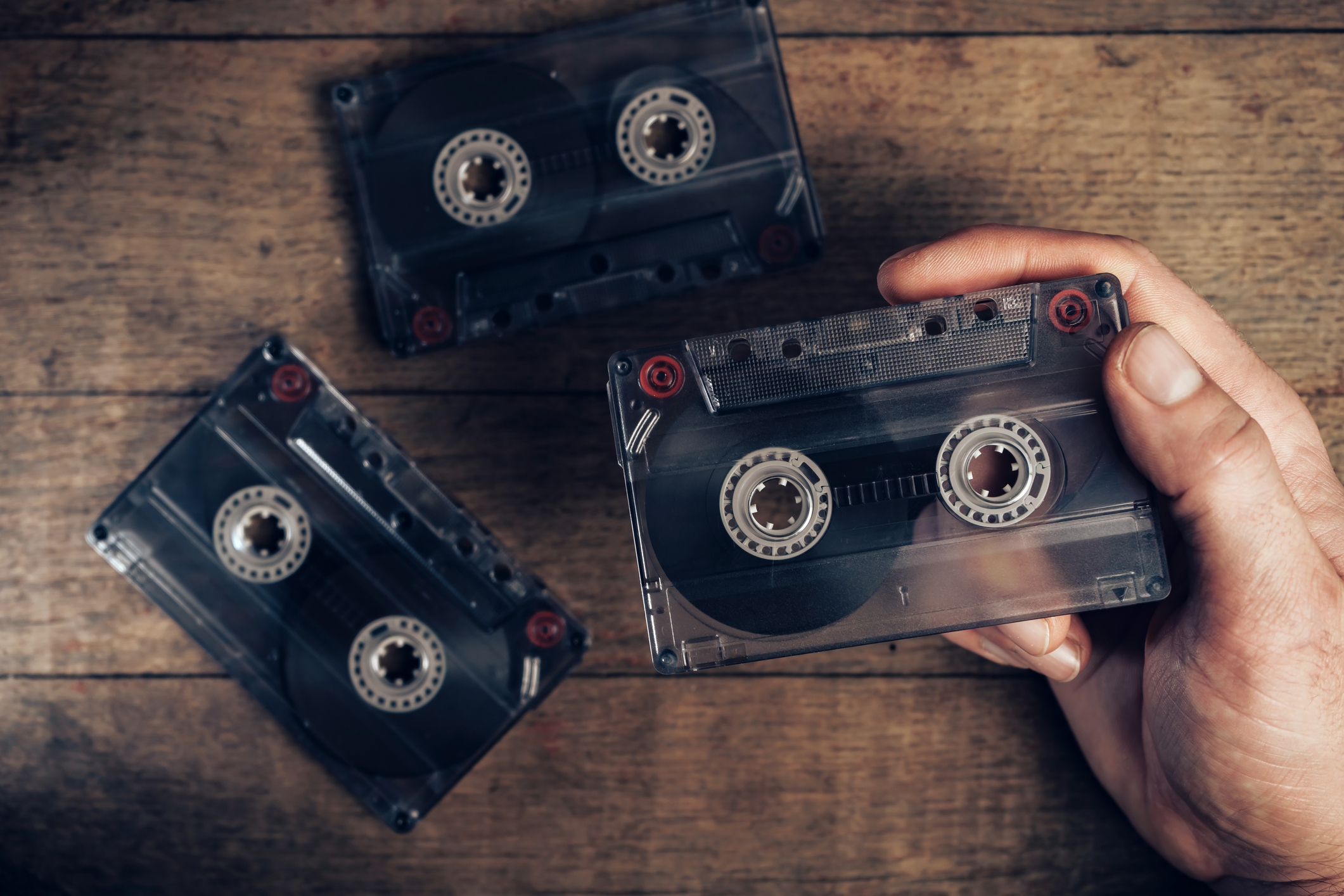 Hand holding audio cassette tape on brown old wooden table. Minimalism retro style concept. Background pattern for design.