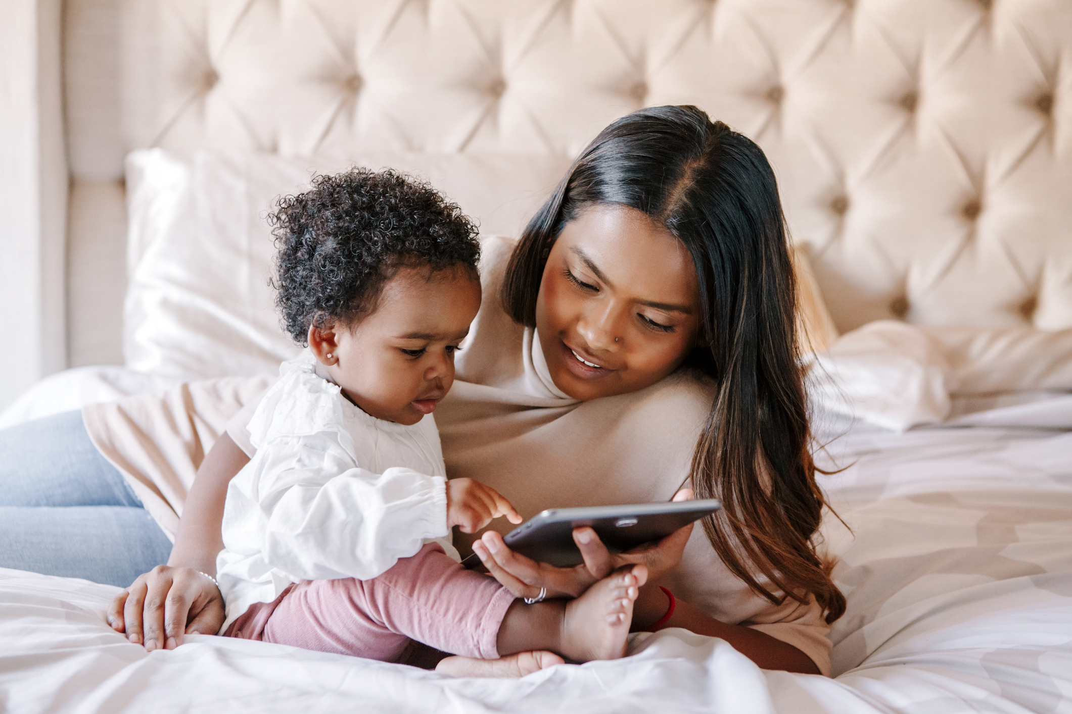 Mixed race Indian black mother with toddler baby girl watching cartoons on a tablet. Ethnic diversity. Family mom with kid using technology. Video chat, video call. Black people community.