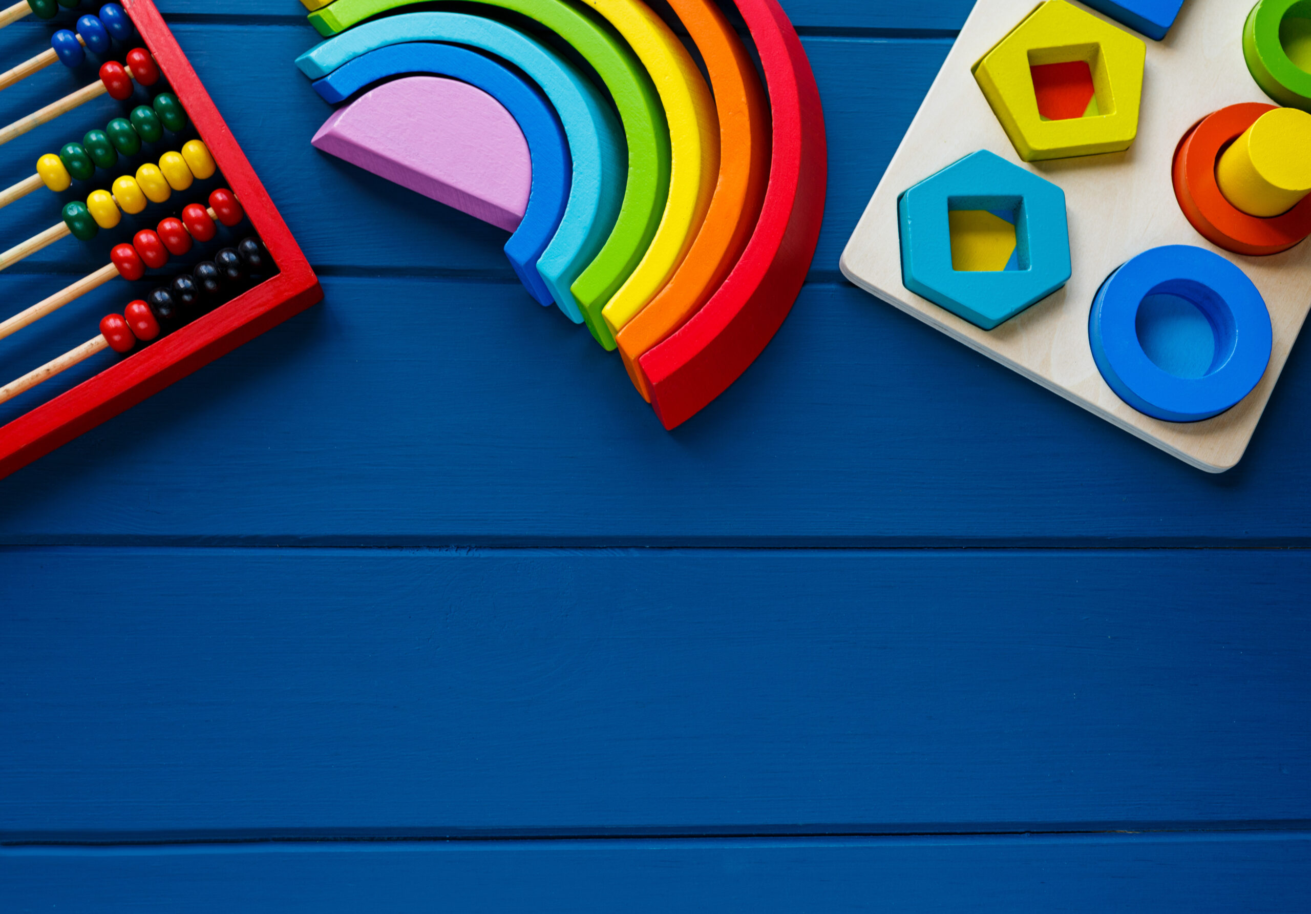 Wooden toys, arc, cubes, brushes on classic blue background. Back to school background. Close up. Top view, copy space. Educational games for kindergarten, preschool kids