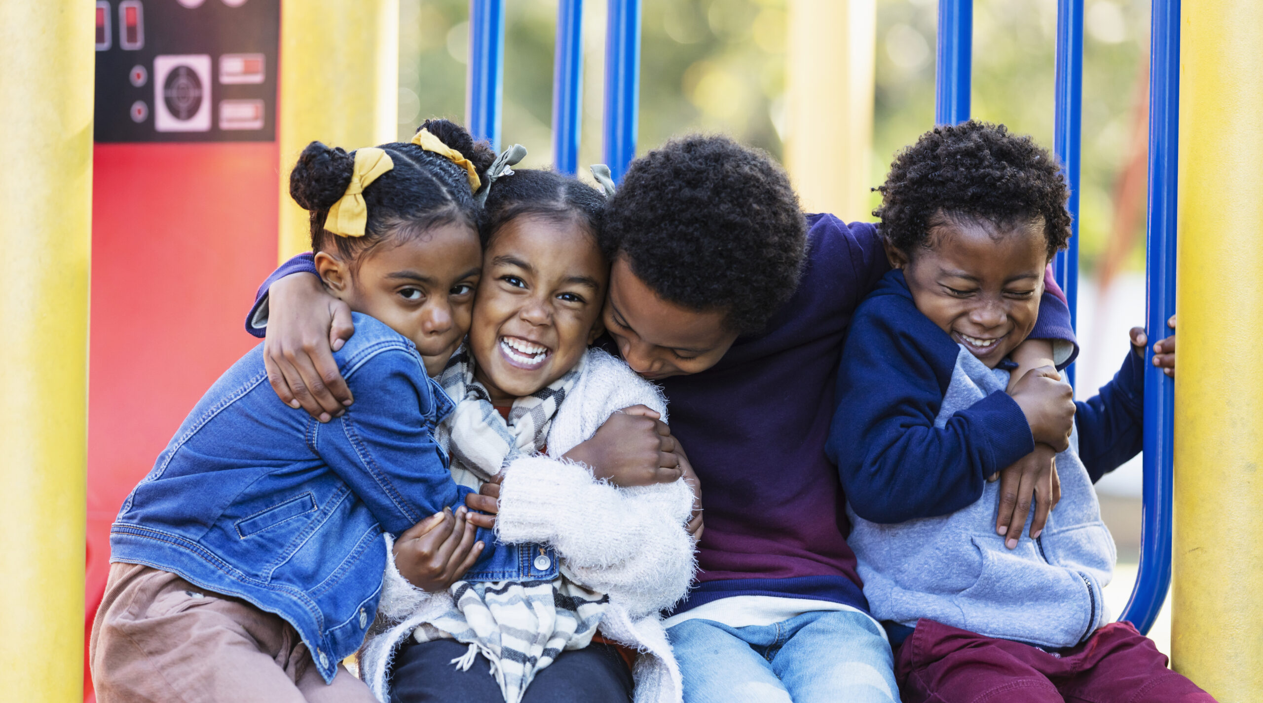 Four young siblings hugging on playground