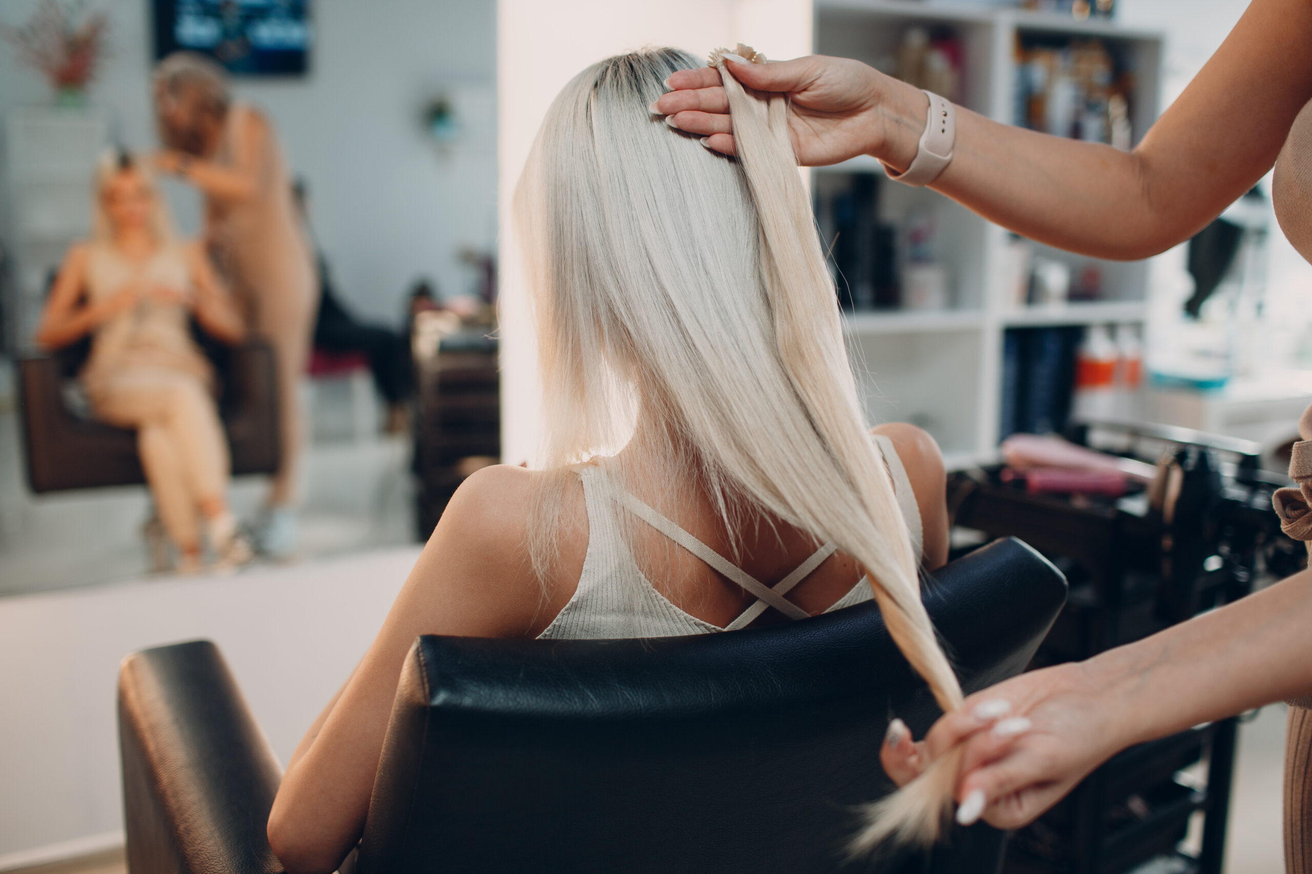 Hairdresser female making hair extensions to young woman with blonde hair in beauty salon. Professional hair extension.