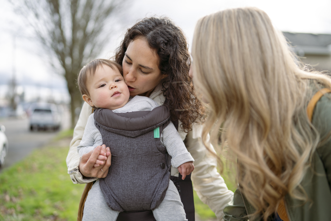 Loving mom giving cute toddler girl a kiss while outside walking in neighborhood