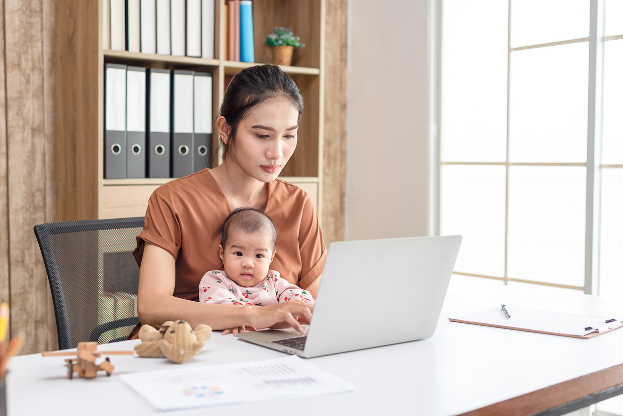 Busy woman trying to work while babysitting newborn baby daughte.  Young beautiful Asian mother holding little baby on lap while another hand typing. Working women with multitasking.