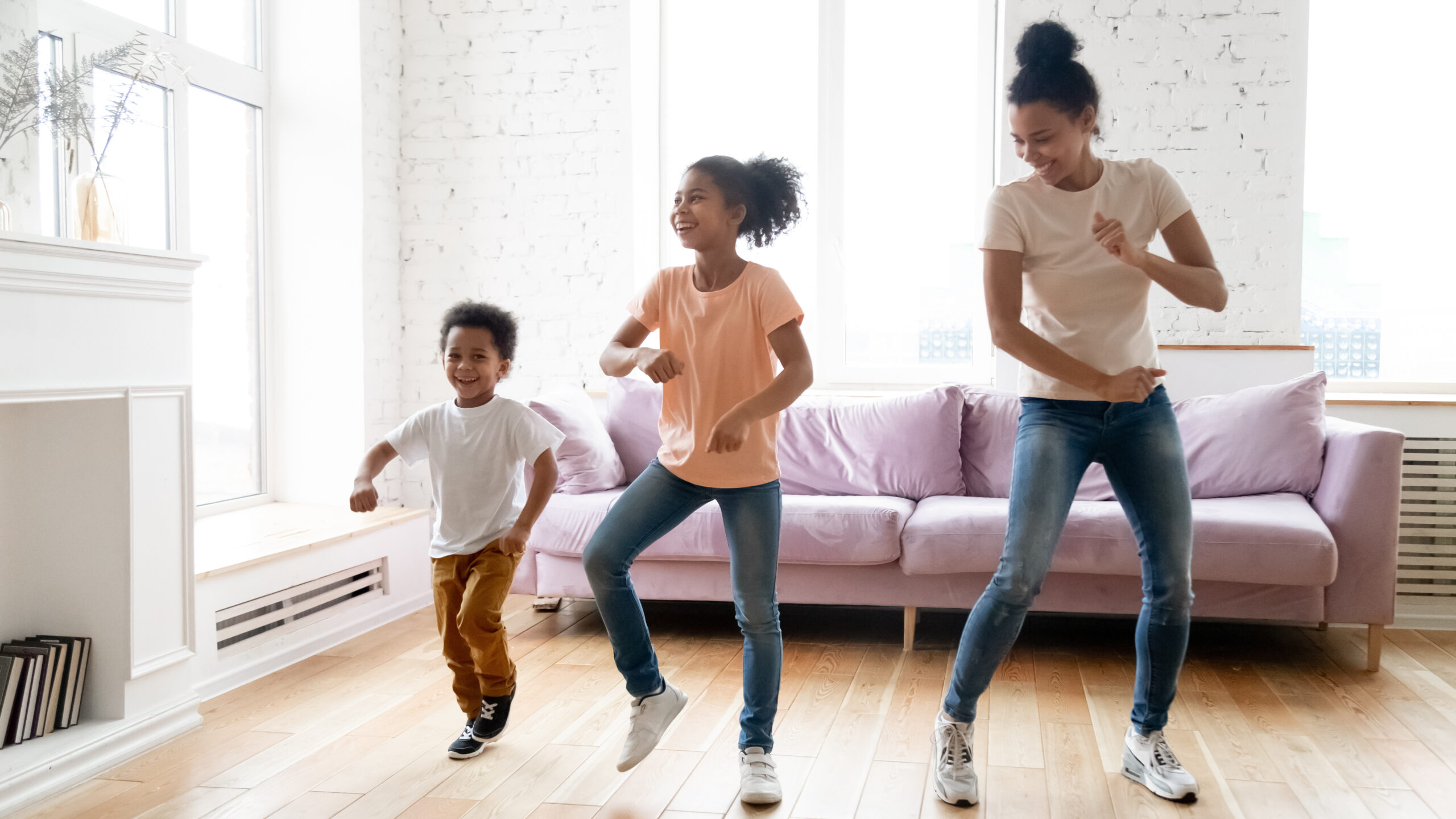 Black children and young babysitter dancing in living room