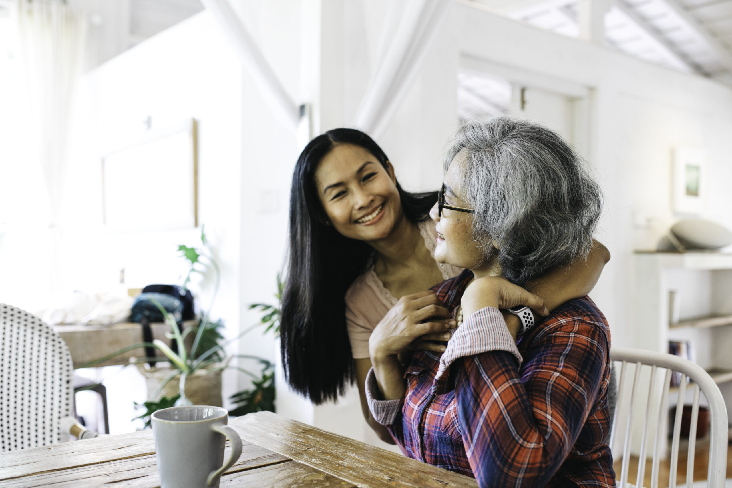 Loving adult daughter embracing cheerful senior mother at home