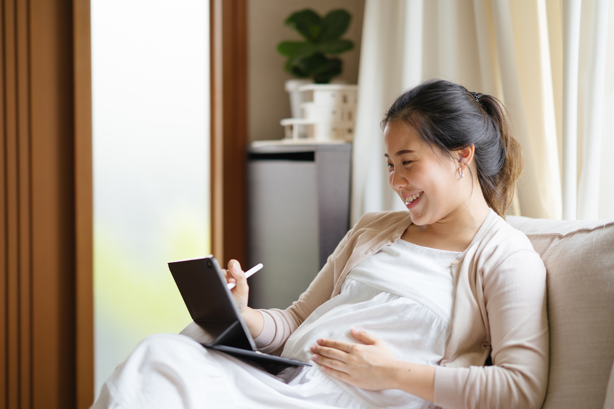 Thoughtful pregnant woman working on digital tablet.