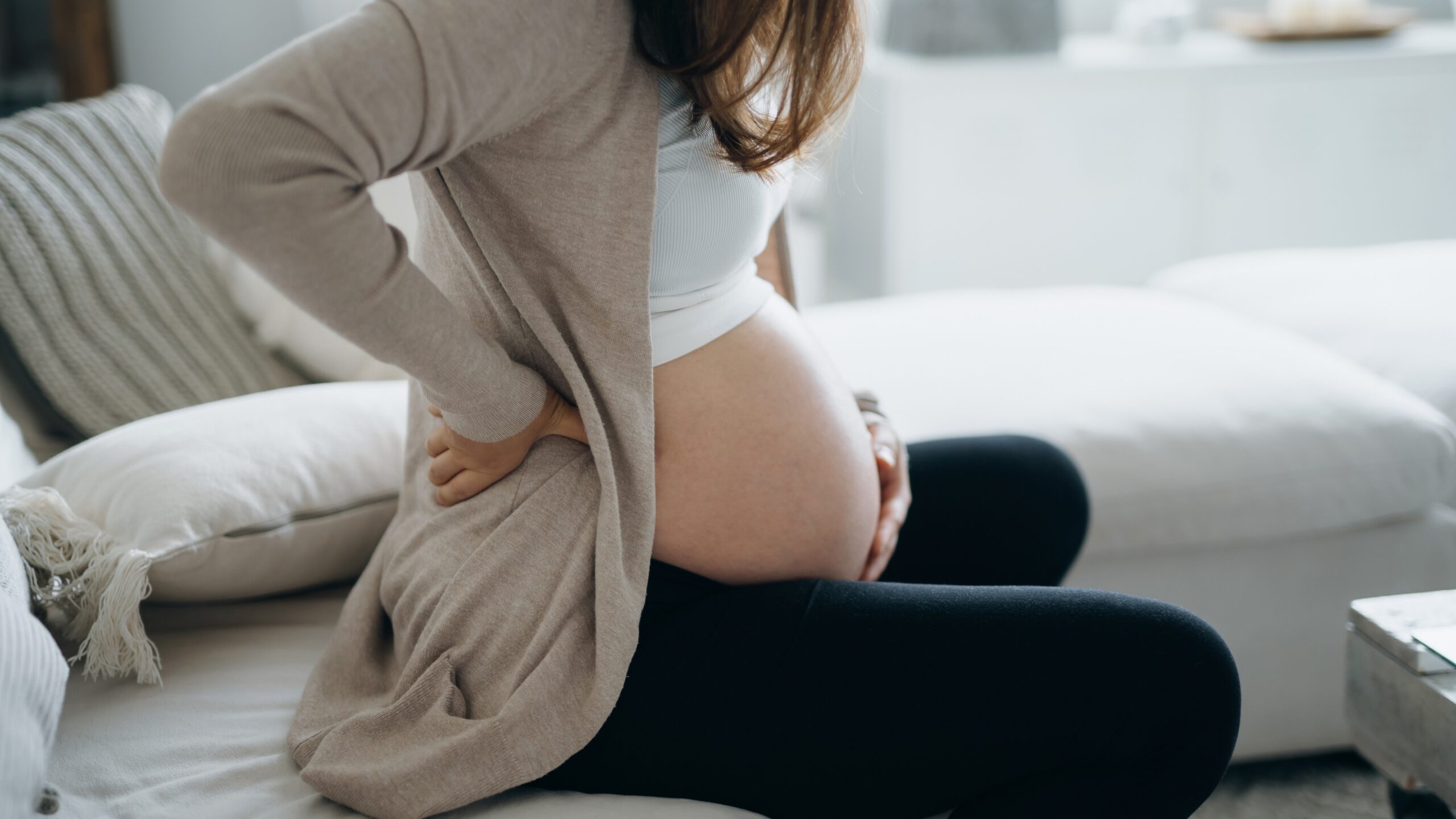 Pregnant woman sitting on couch holding her stomach