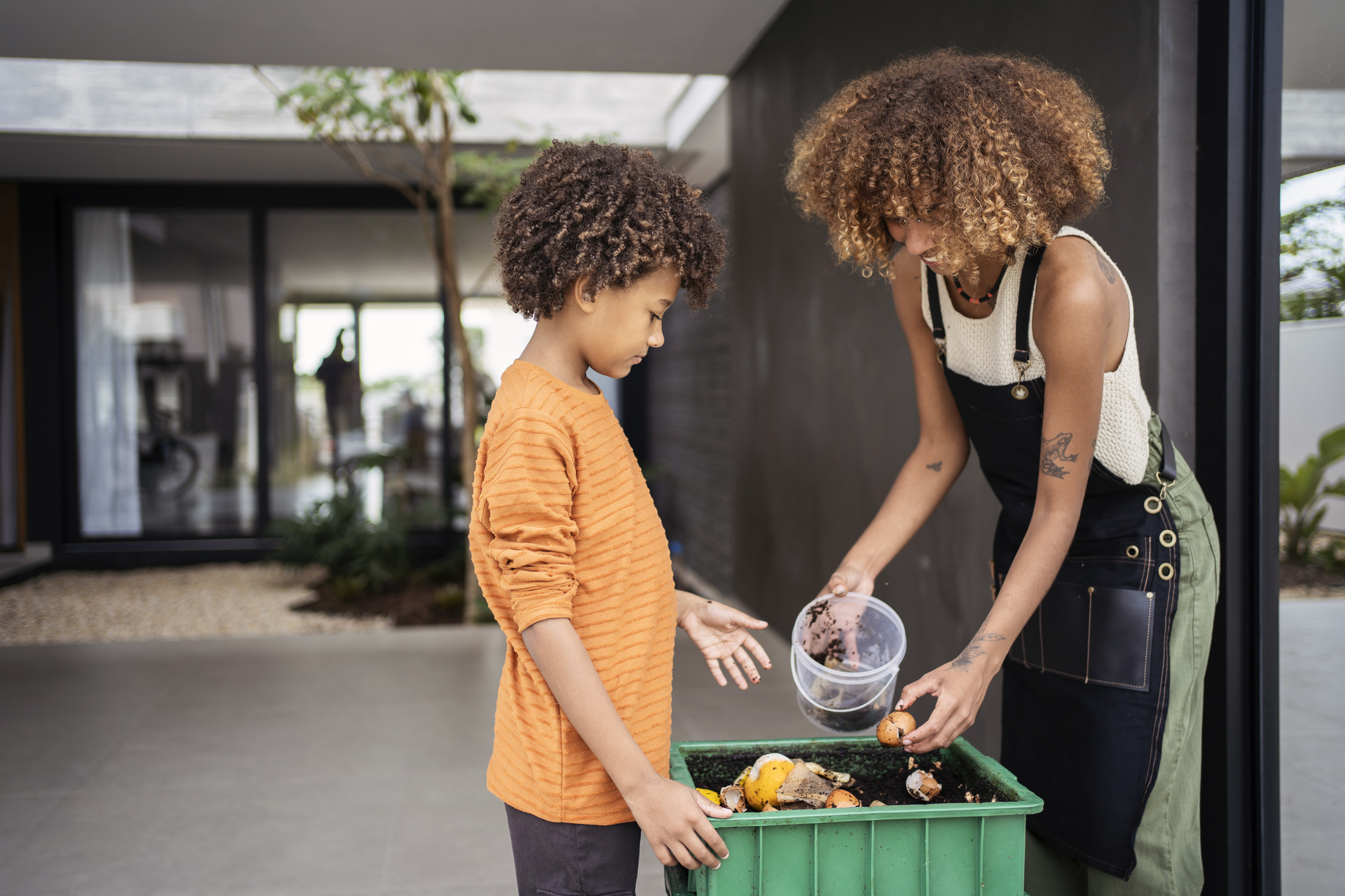 African american young woman and her younger brother making compost from leftovers. Sustainability concept.