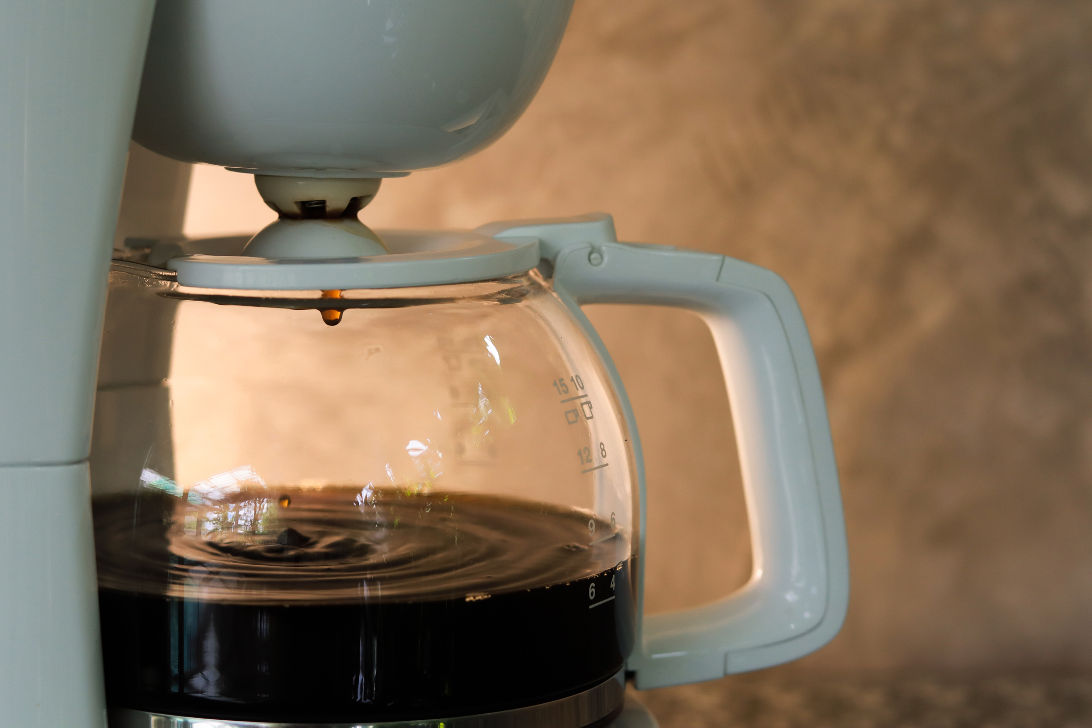 Coffee pot with coffee dripping inside on gray concrete background and warm light. Copy space.