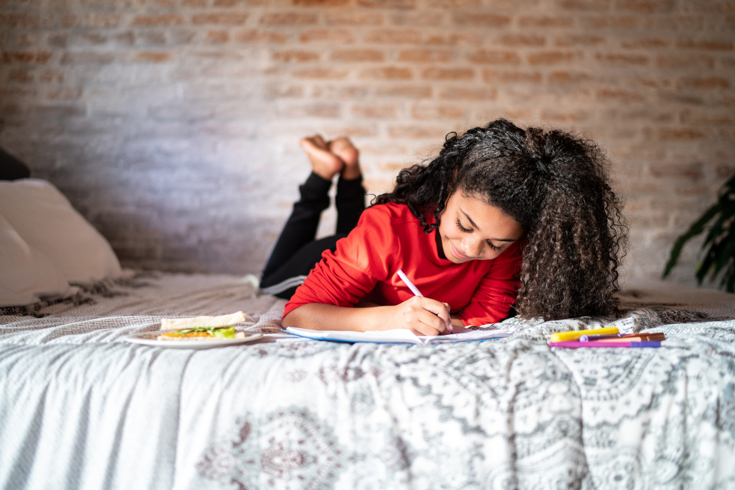 Girl writing on note pad or dairy lying on bed at home