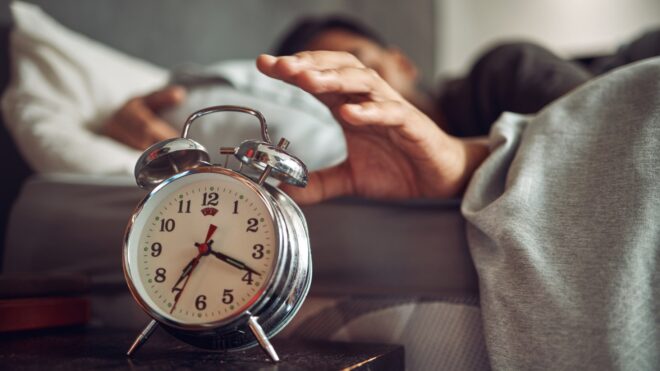 Sleeping man turning off alarm clock