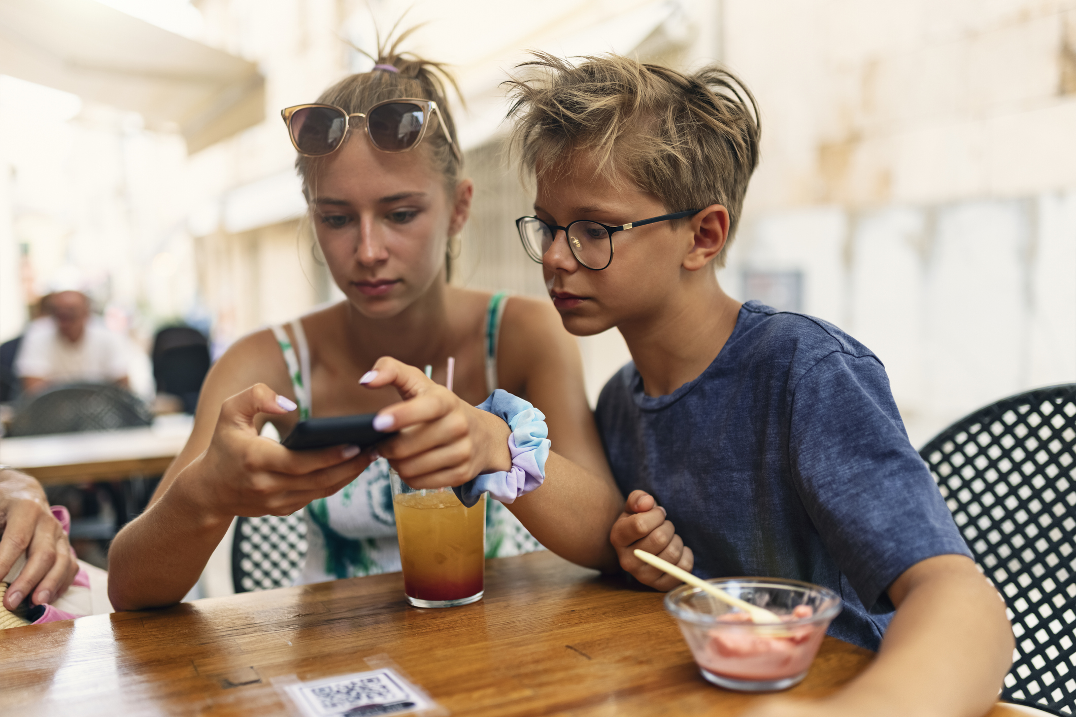 Brother and sister checking mobile menu at sidewalk café in Alcudia, Majorca, Spain