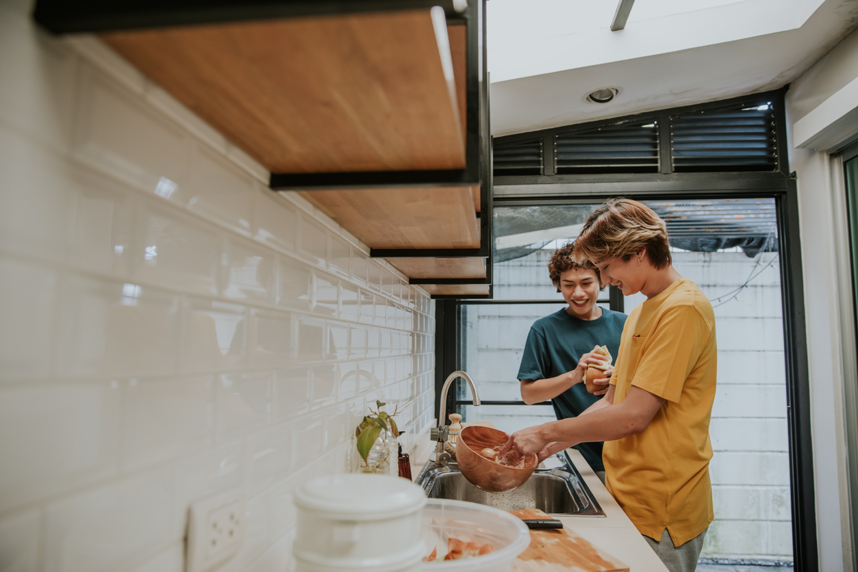 Everyday sustainable life of LGBTQIA people cleaning wooden dish with eco dish brush beside his friend at home-stock photo