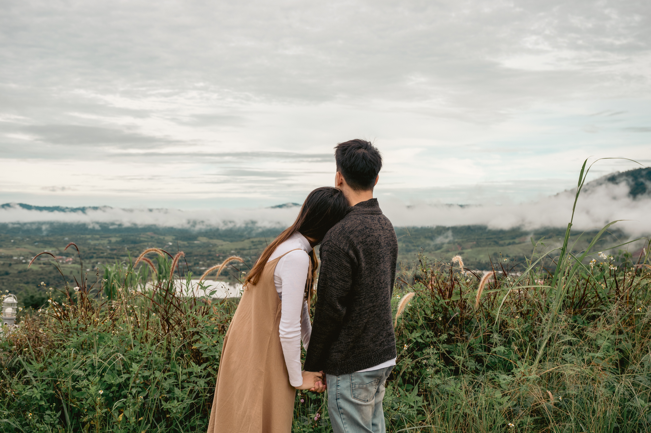 Asian couple stand embracing and holding hands looking at view among the nature on vacation