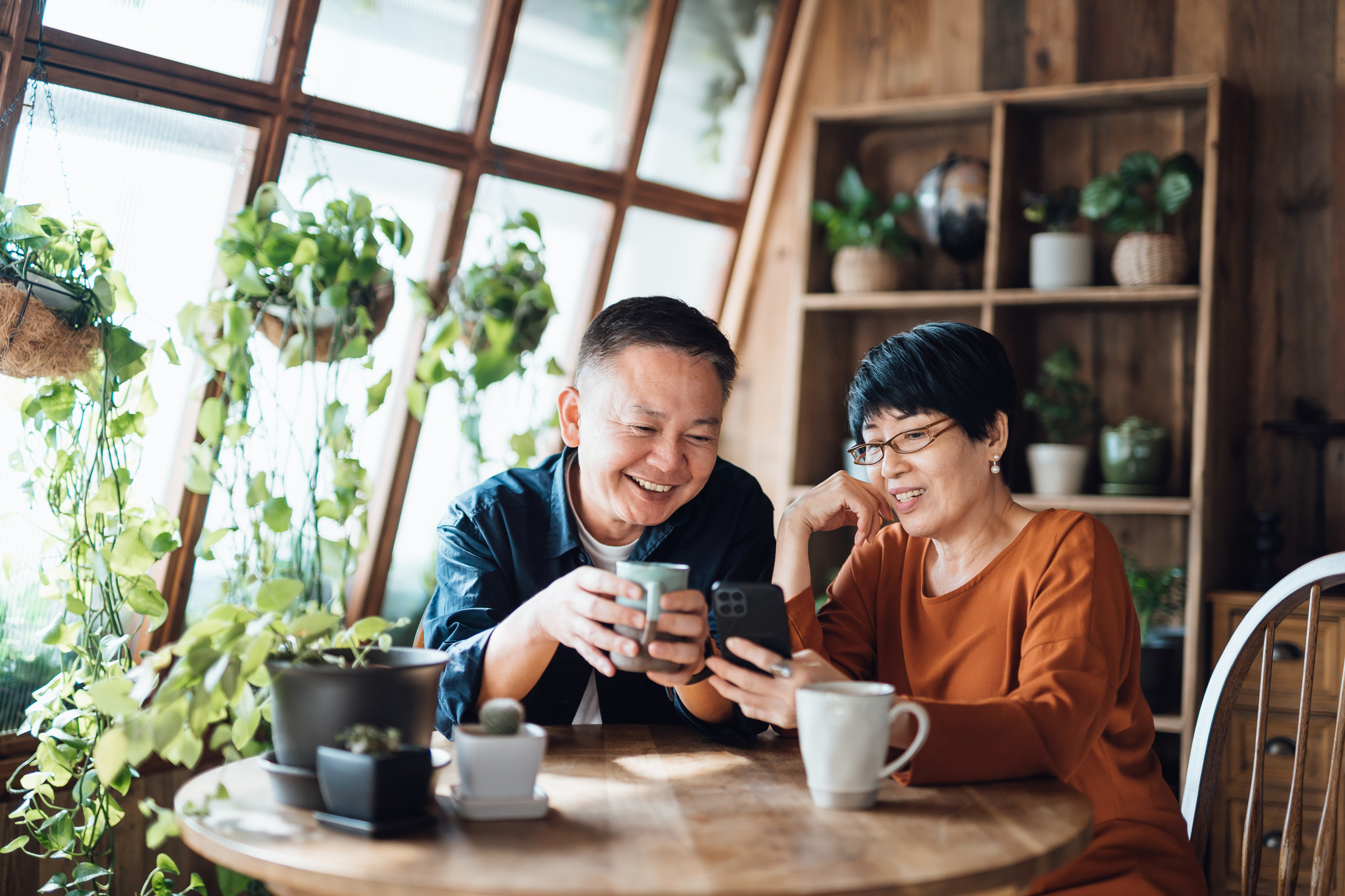 Happy senior Asian couple video chatting, staying in touch with their family using smartphone together at home. Senior lifestyle. Elderly and technology