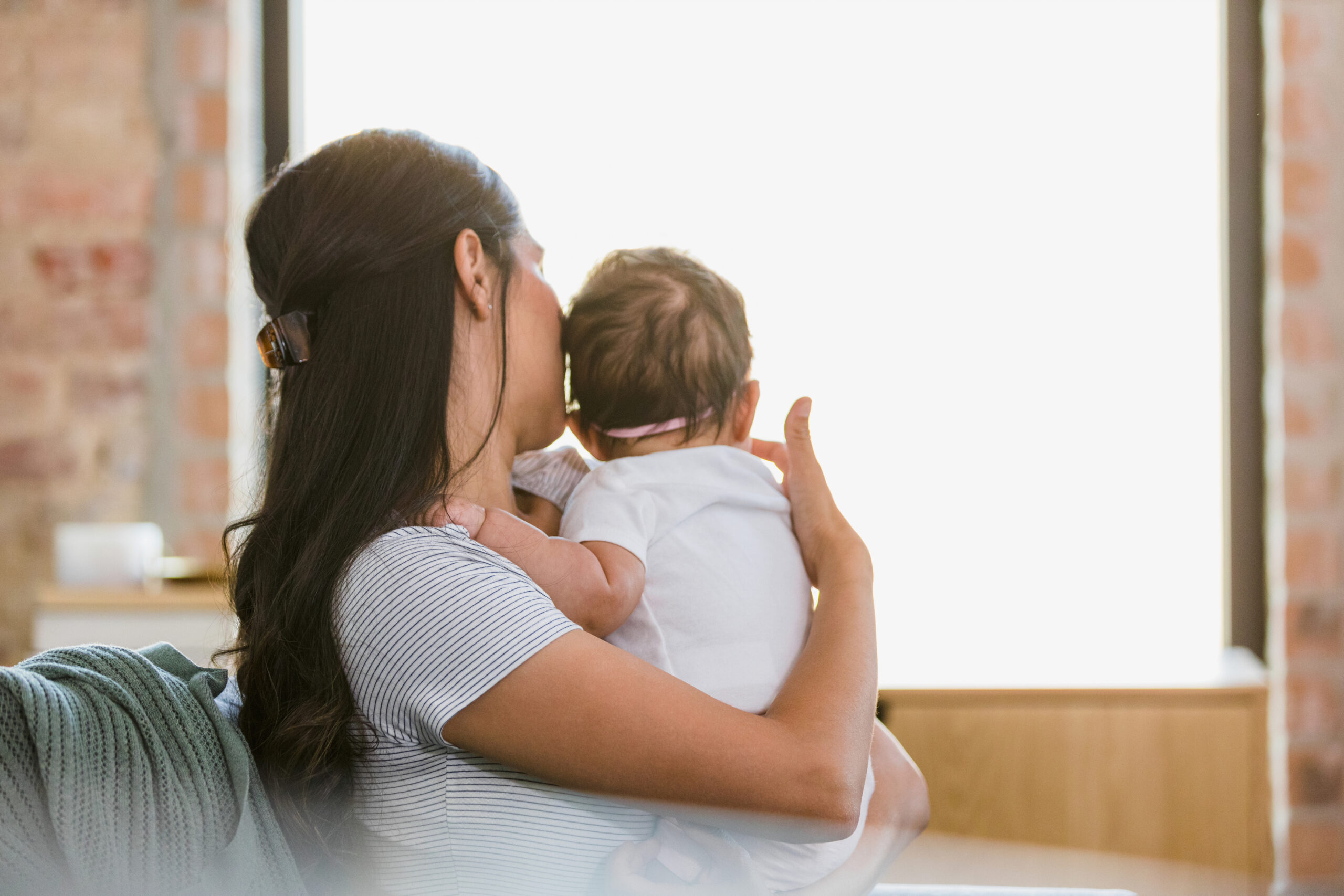 Mother and baby daughter both look out living room window