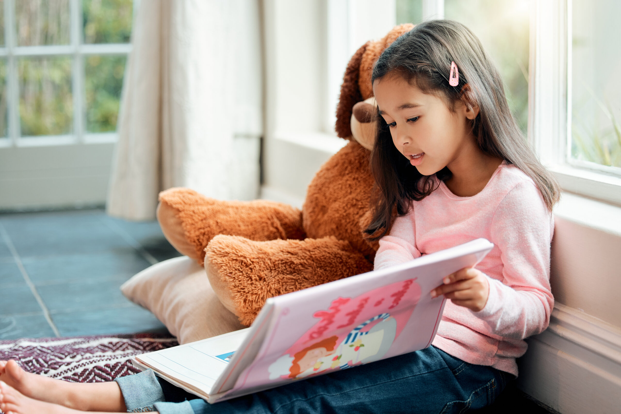 Shot of a little girl reading a book at home