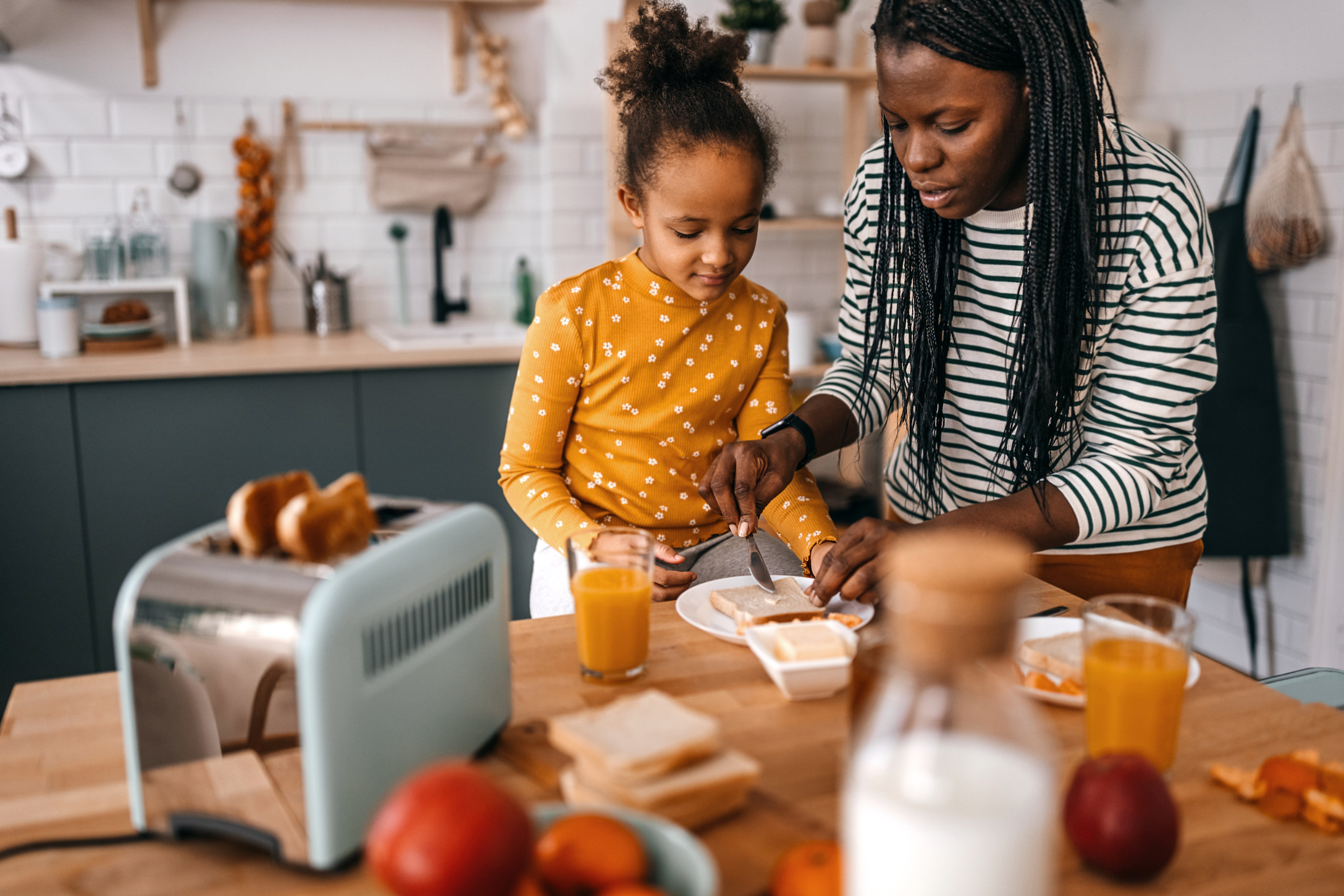 Mother and daughter making breakfast on dining table in kitchen