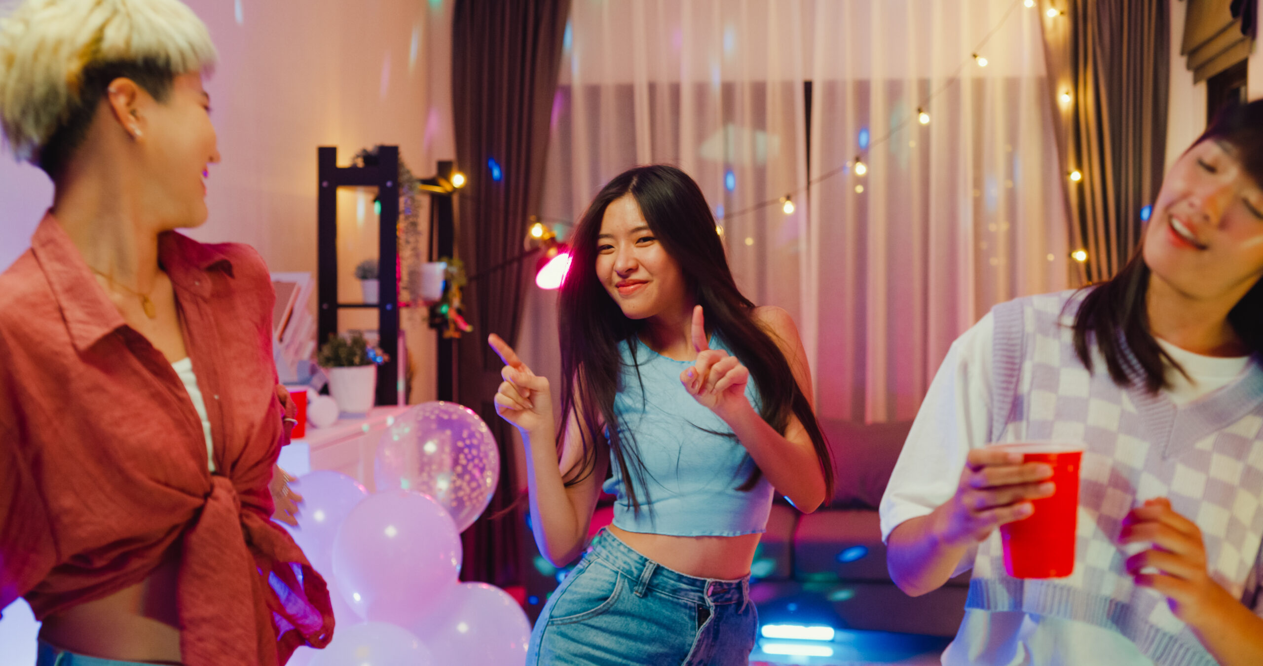 Young Asian female friends dancing having fun at colorful house party at night.