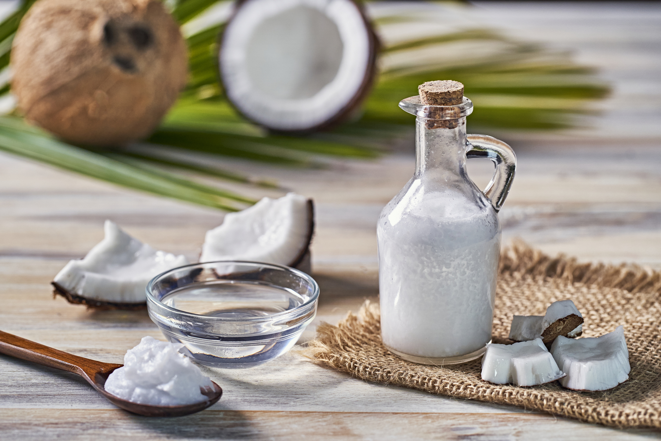 Glass bottle of coconut oil and fresh coconut fruit on wooden rustic white background