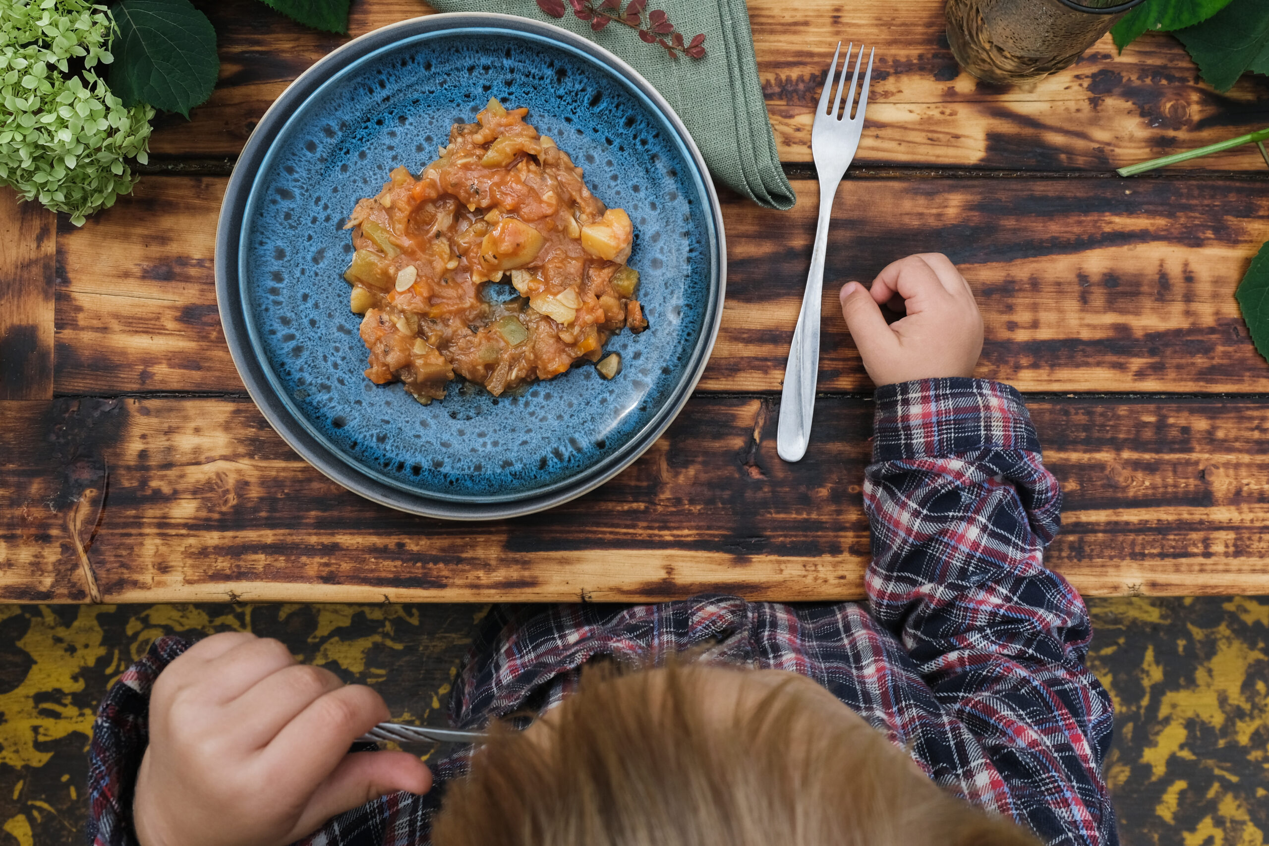 Toddler boy eating vegetable stew. Dining al fresco, table top view.