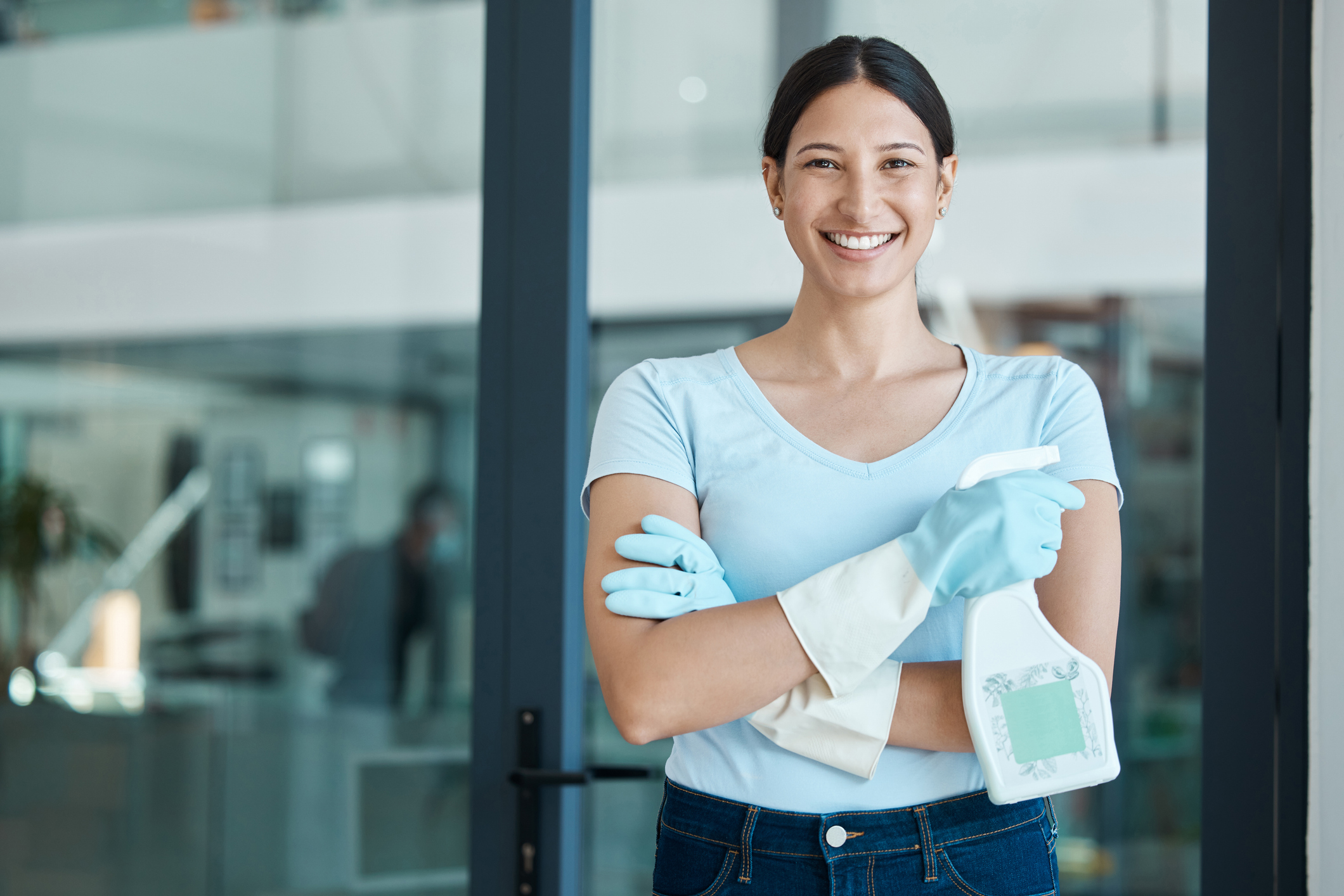 Cleaning service, portrait and cleaner in an office with spray bottle of disinfectant, bleach or detergent. Happy, smile and young female worker with gloves and soap liquid done washing glass windows