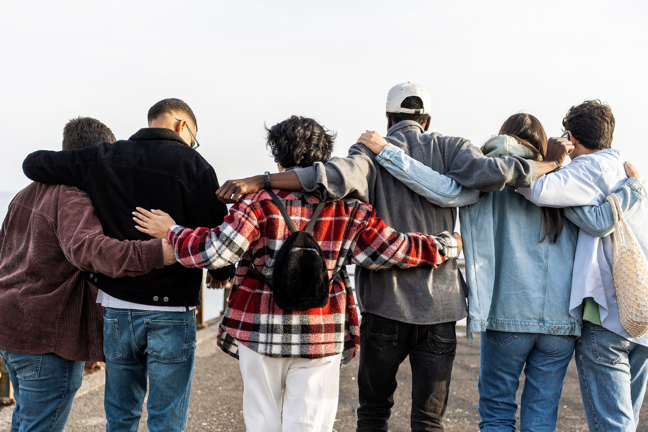 Unite group of multiethnic young friends walking outdoors hugging together