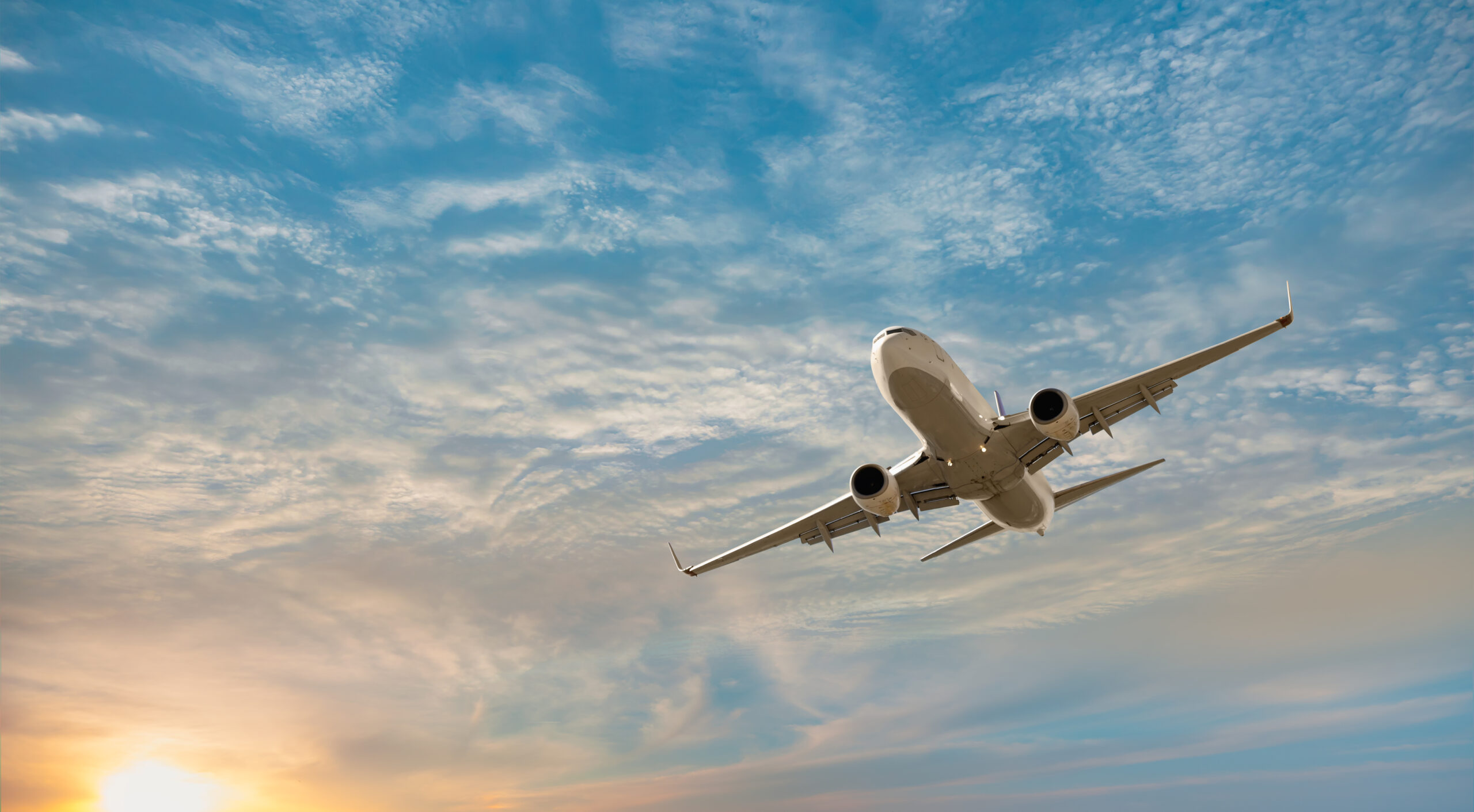 Airplane flying over tropical sea at sunset