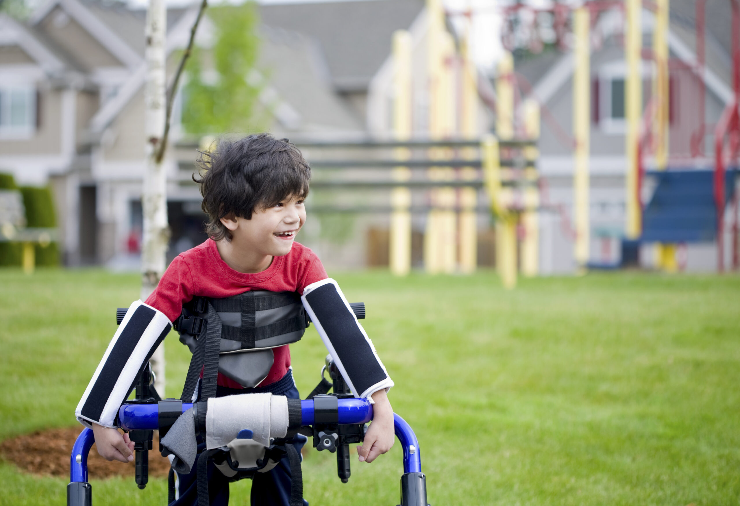 Disabled four year old boy standing in walker by playground