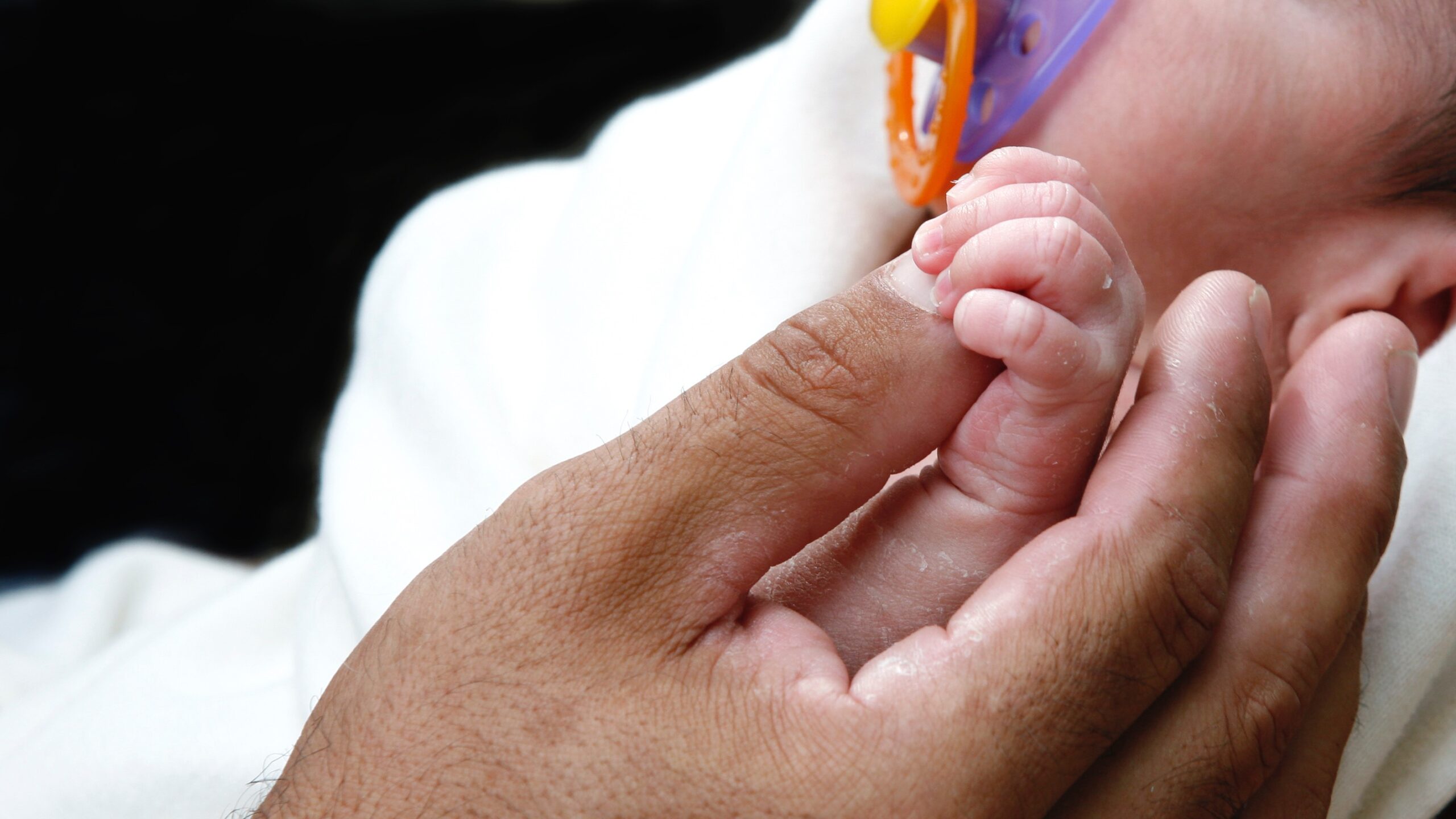 Father holding premature newborn hand