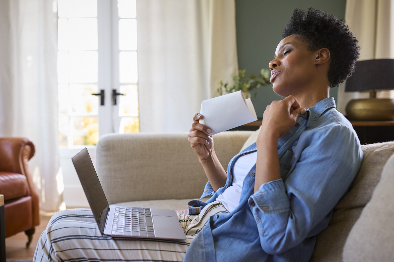 Menopausal Mature Woman At Home With Laptop Having Hot Flush Fanning Herself