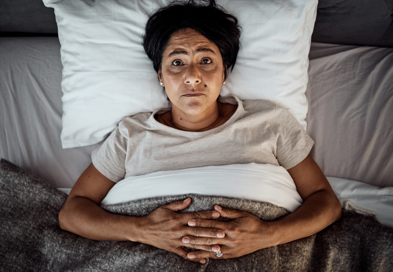 Insomnia, portrait and senior woman in bed from above with menopause, anxiety or stress in her home. Top view, face and elderly female in a bedroom with depression, trauma or mental health crisis