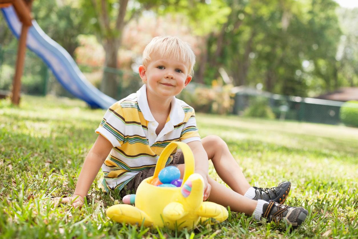 Little Boy With Toy Basket Sitting On Grass At Park