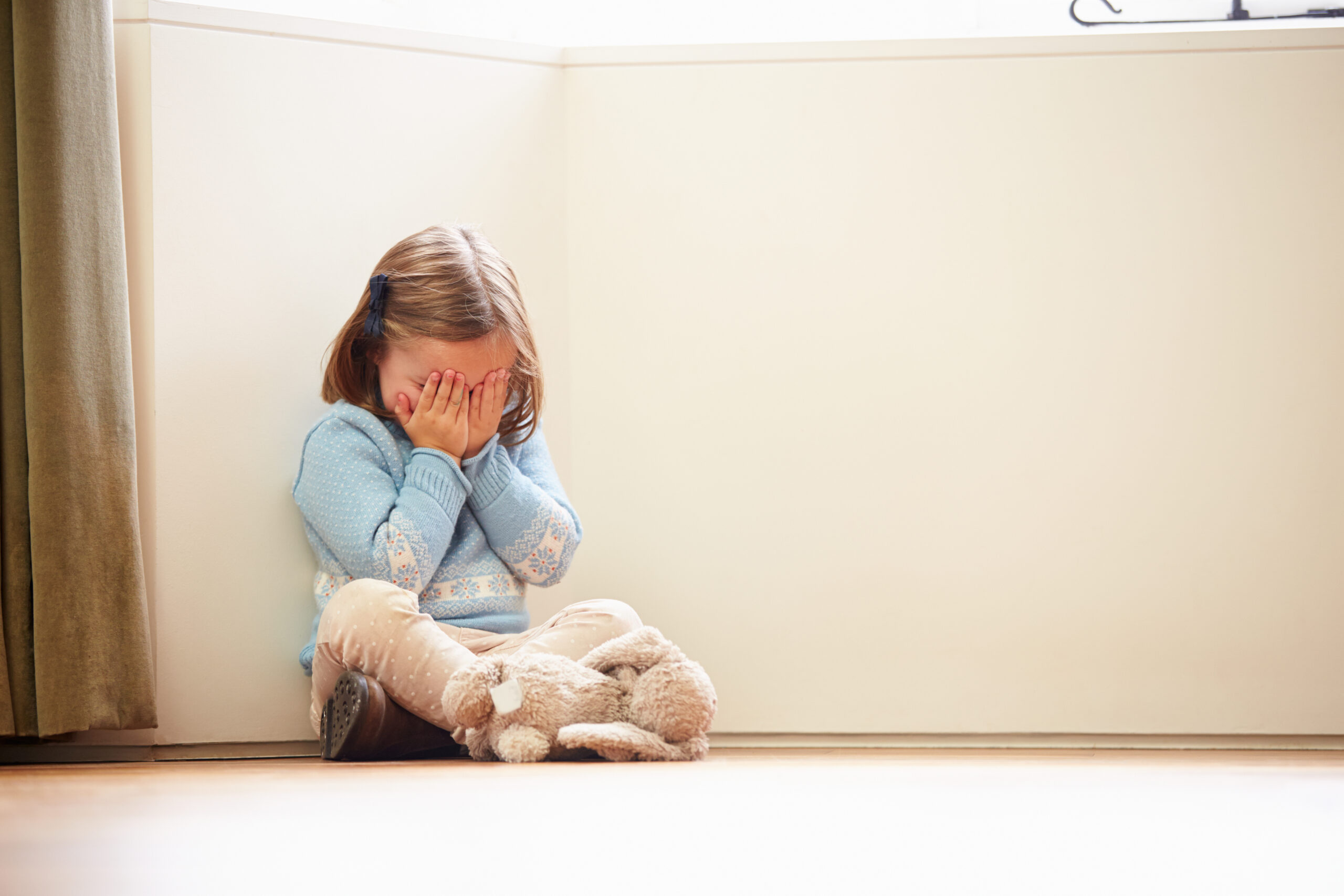 A girl sits at a corner, covering her face with her hands