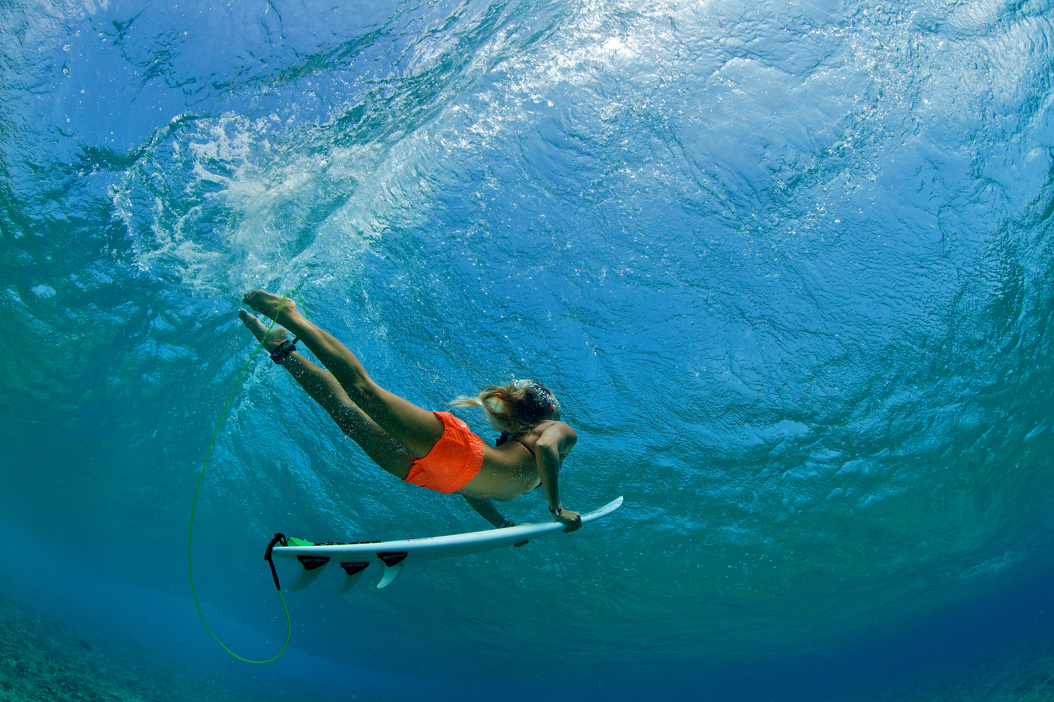 Surfer girl in orange shorts duck dives a wave