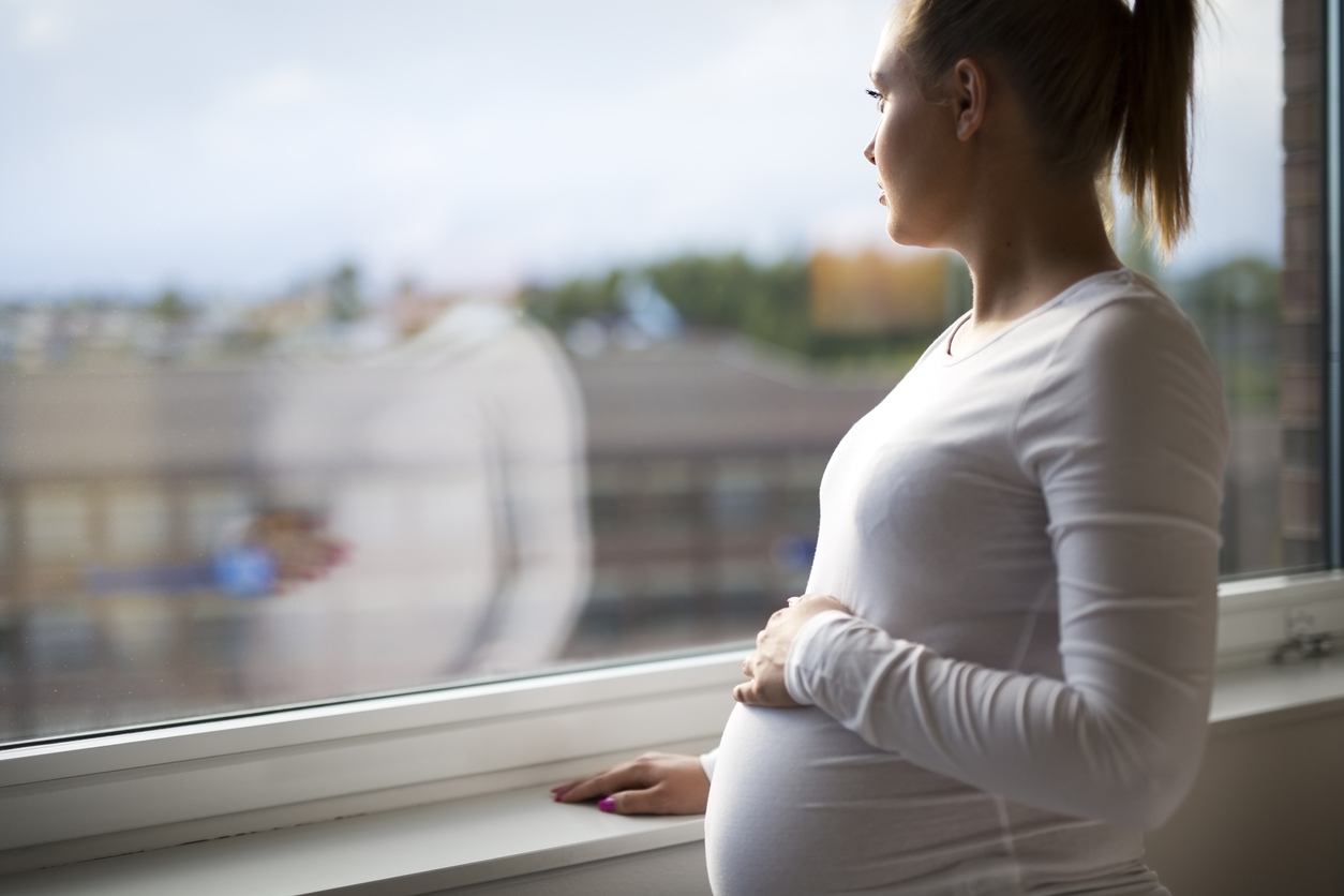 Thoughtful pregnant woman looking out the window