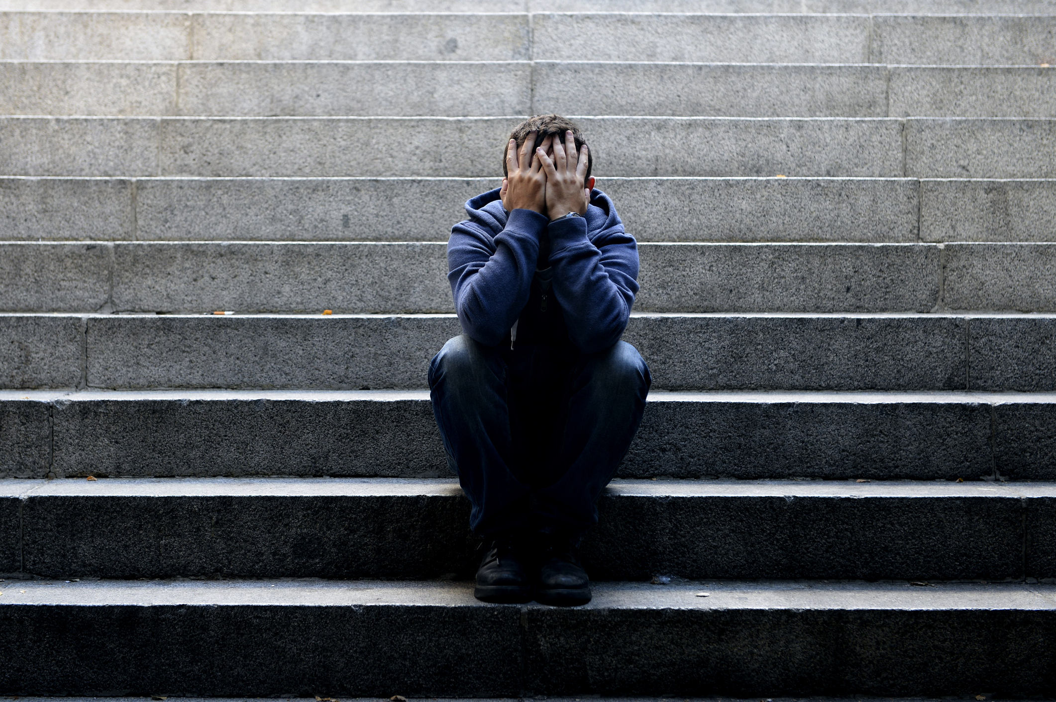 Young man suffering depression sitting on ground street concrete stairs