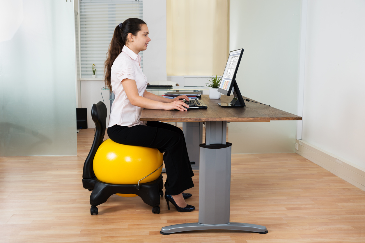 Businesswoman Sitting On Fitness Ball With Computer At Desk