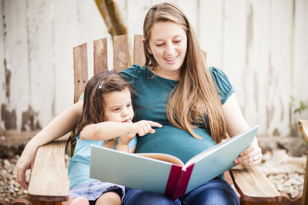 Pregnant Woman Reading to Daugther in Backyard