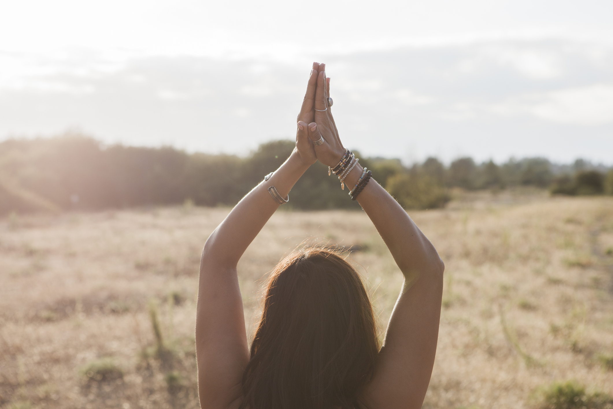 Woman meditating with hands clasped overhead in sunny rural field