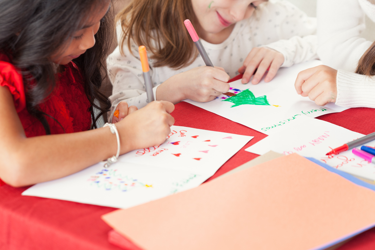 Young girls writing Christmas cards for charity shoe boxes