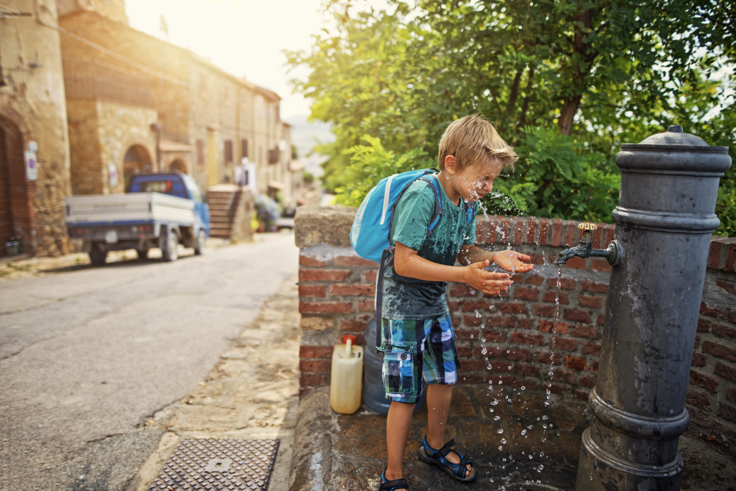 Little tourist splashing face with water from public fountain