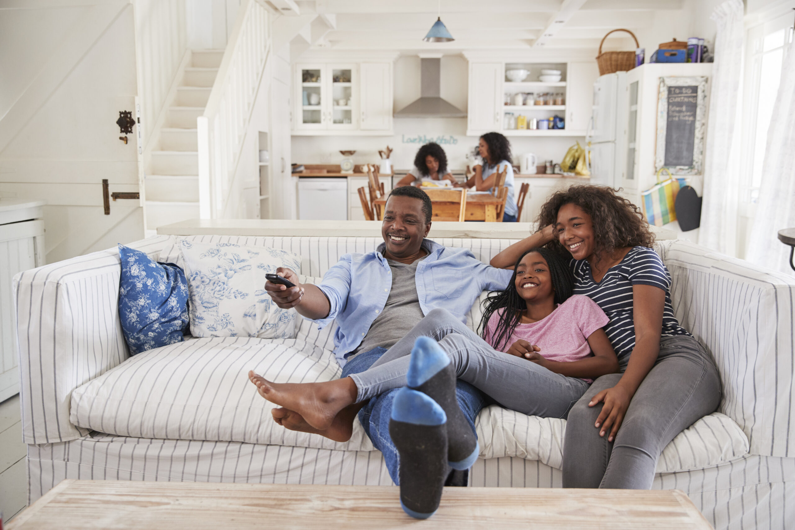 Father Sitting On Sofa Watching TV With Teenage Daughters