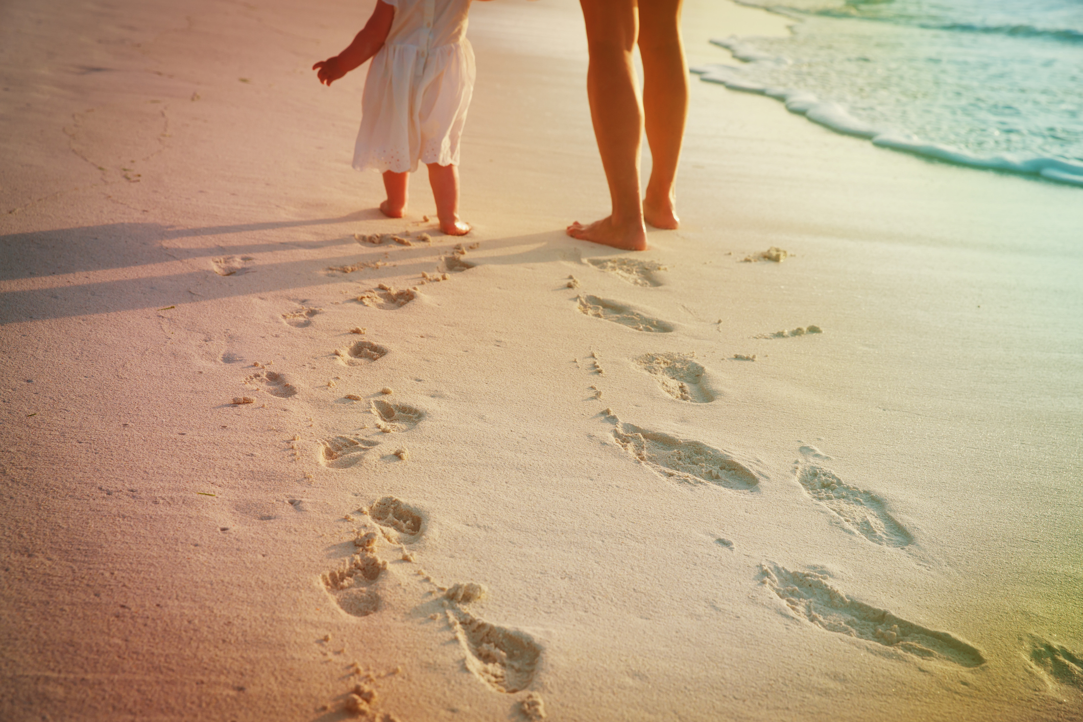 mother and daughter walking on beach leaving footprint in sand