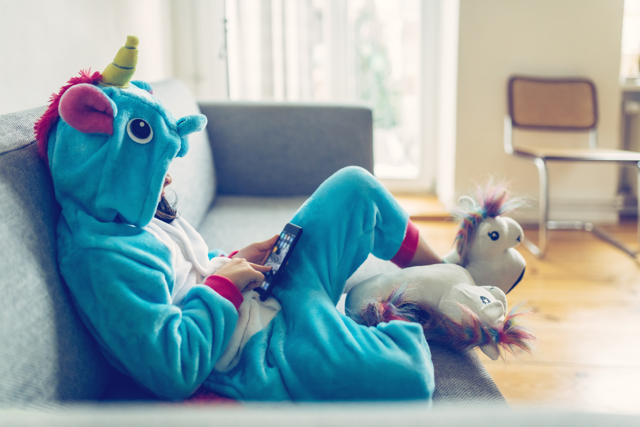 little girl in unicorn costume with mobile on couch